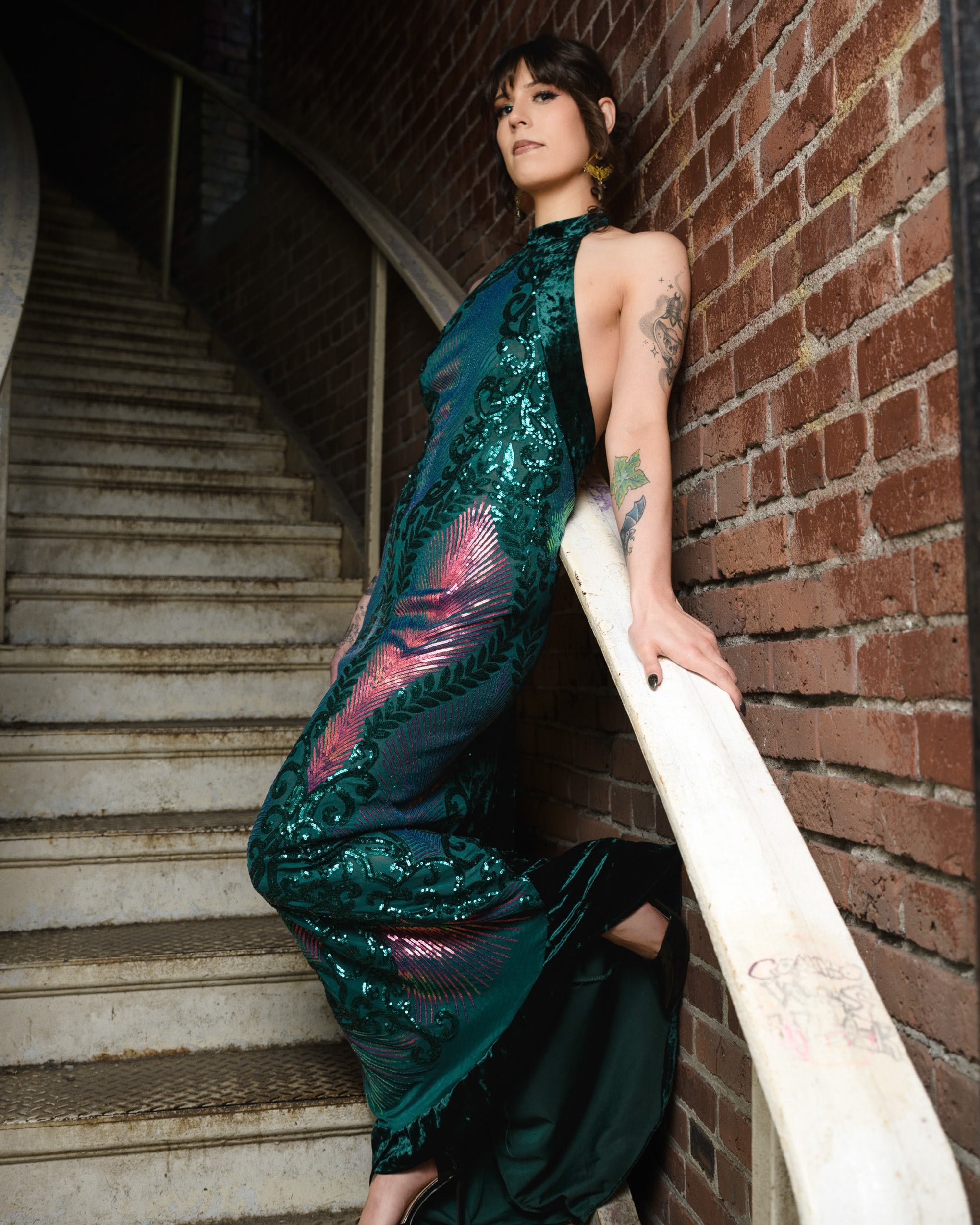 Woman in a green sequined dress leaning against a brick wall. [color_id:green-purple] [editorial]