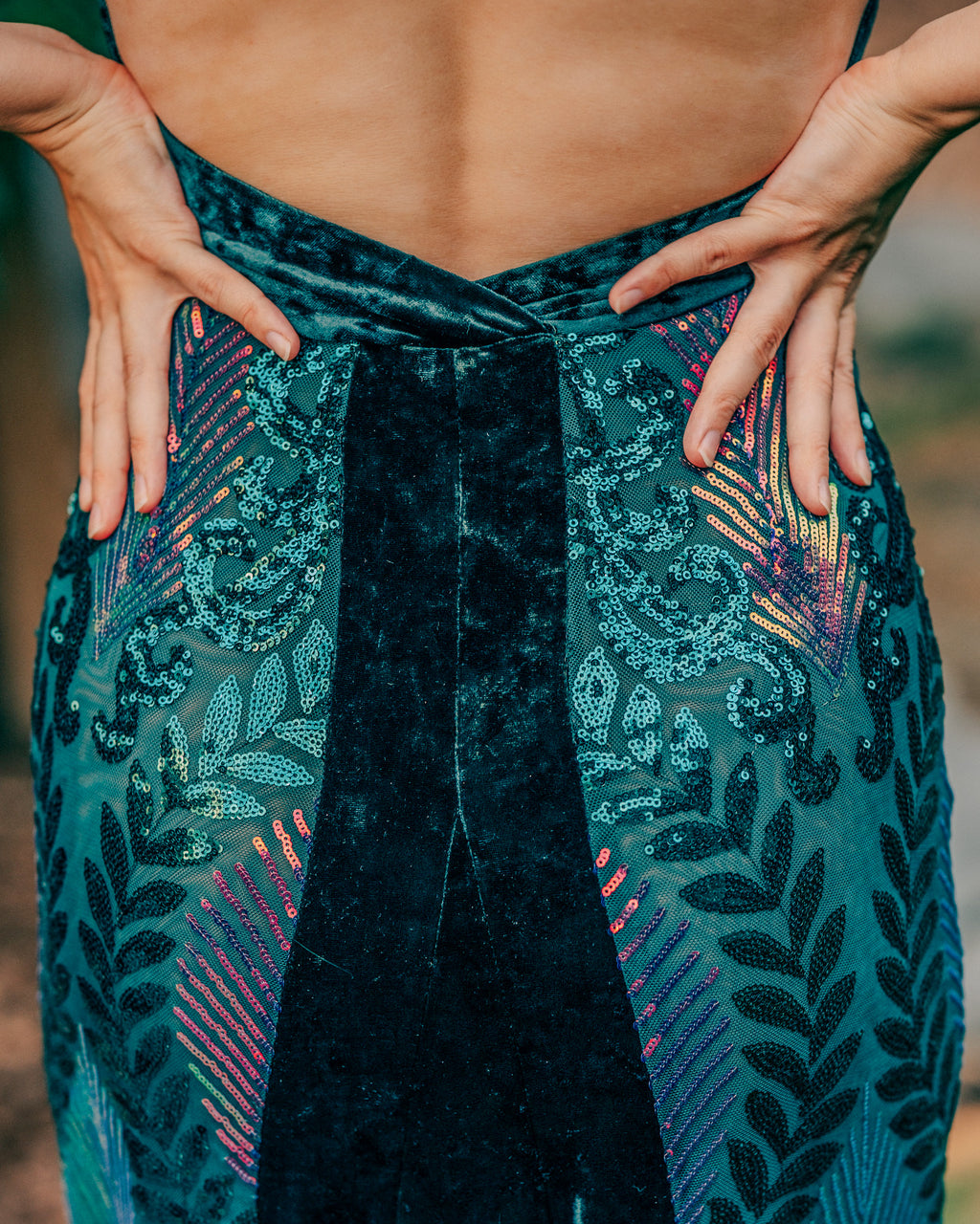 Person wearing a teal patterned garment with their hands on hips against a blurred natural background
  [model_size:S]  [dress_size:S]  [color_id:green-purple] [editorial]