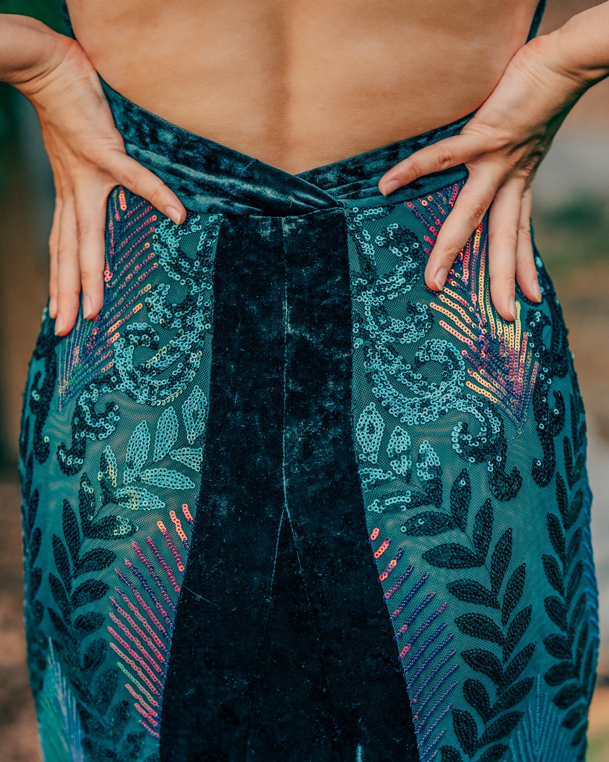 Person wearing a teal patterned garment with their hands on hips against a blurred natural background
  [color_id:green-purple] [editorial]