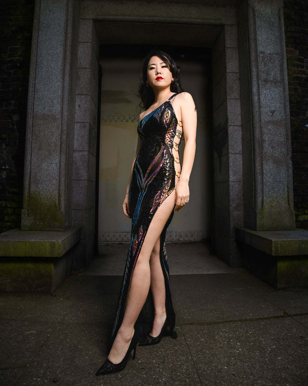 Woman in a glamorous evening gown standing in a stone archway  [model_size:XS]  [color_id:black-lavender] [editorial]