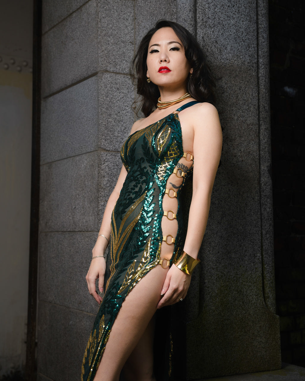 Woman in a green and gold dress standing against a gray wall.  [model_size:XS] [color_id:green-gold] [editorial]