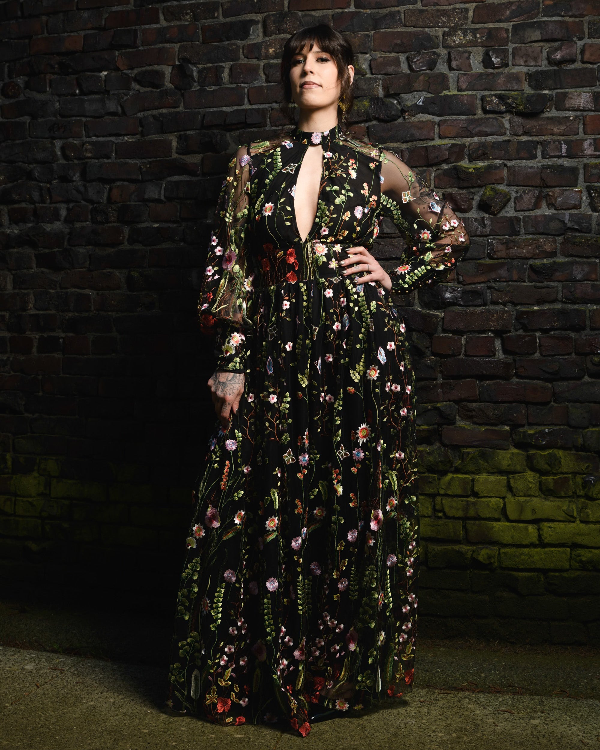 Woman in a floral dress standing against a brick wall. [color_id:black] [editorial] 