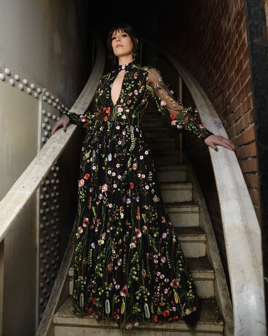 Woman in a floral dress standing on a staircase [color_id:black] [editorial] [model_size:M] [dress_size:L]