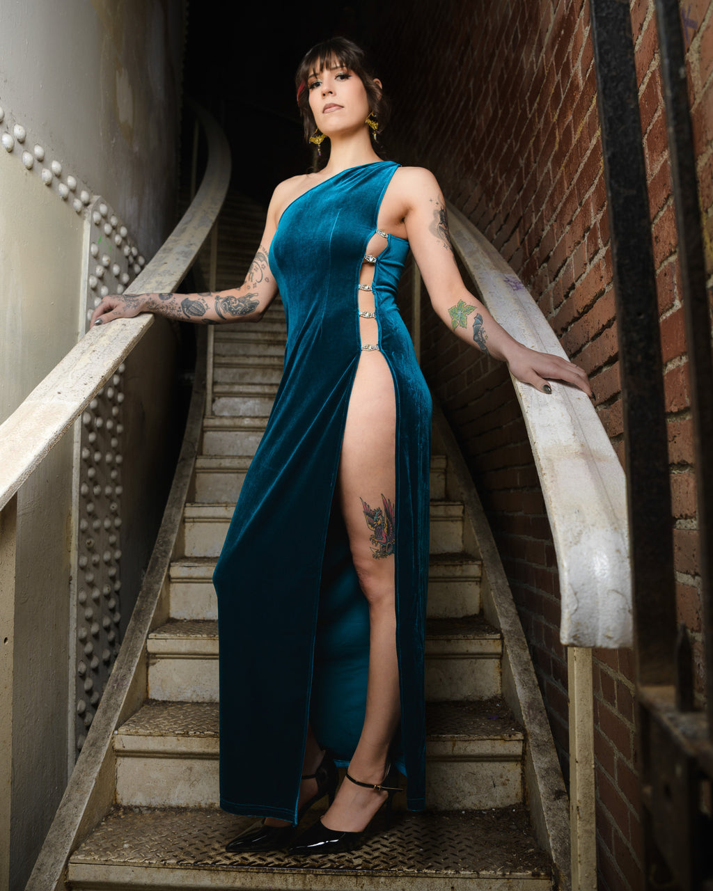 Woman in a teal dress with a high slit standing on a staircase. [color_id:royalty-blue] [editorial] [hero] [model_size:M] 