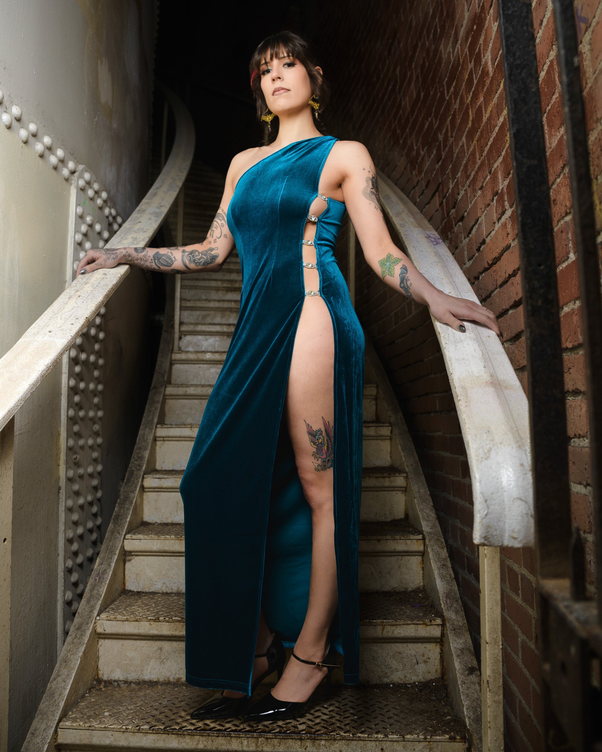 Woman in a teal dress with a high slit standing on a staircase. [color_id:blue] [editorial] [hero]