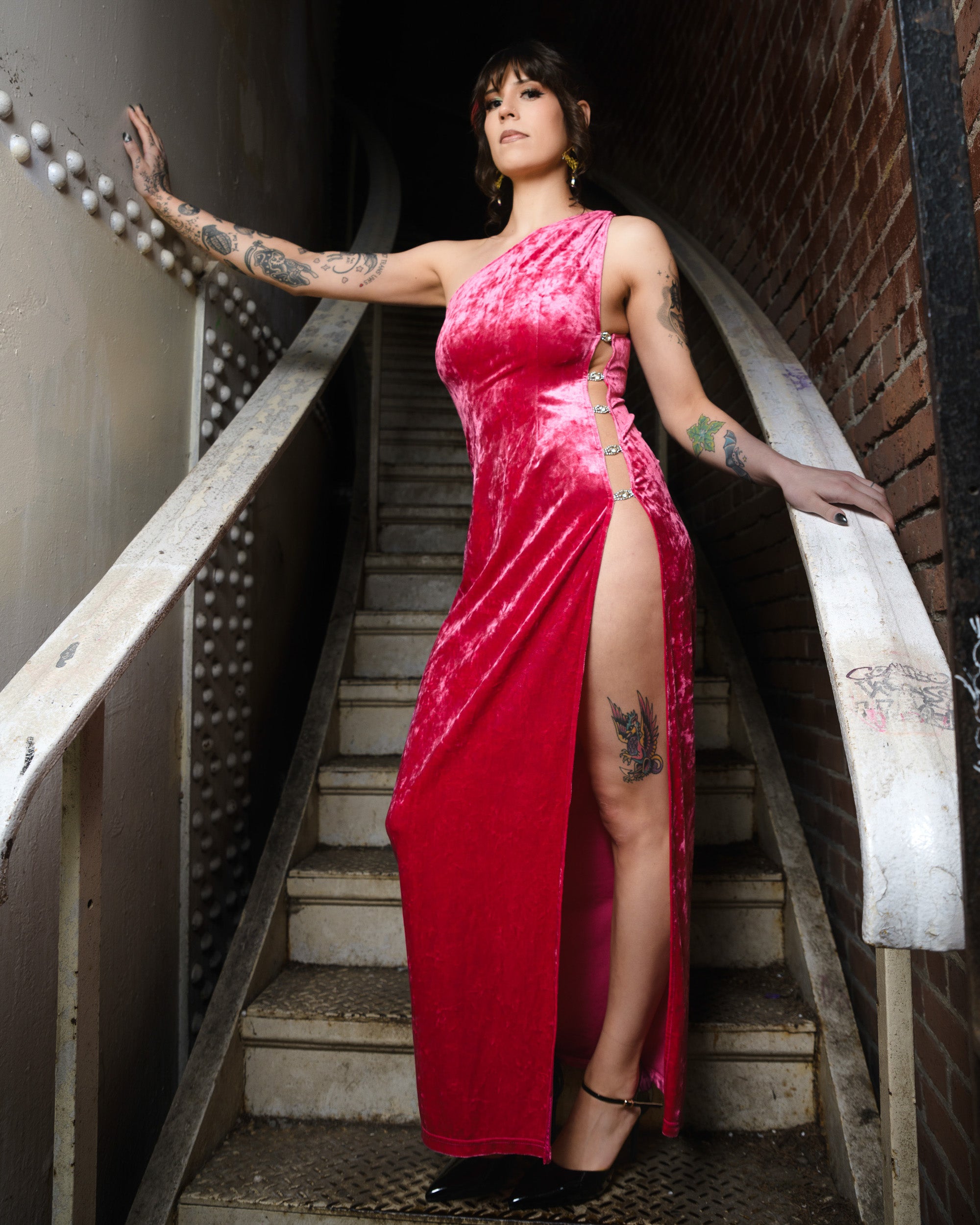Woman in a pink dress standing on a staircase with tattoos visible. [color_id:pink] [editorial] [hero]