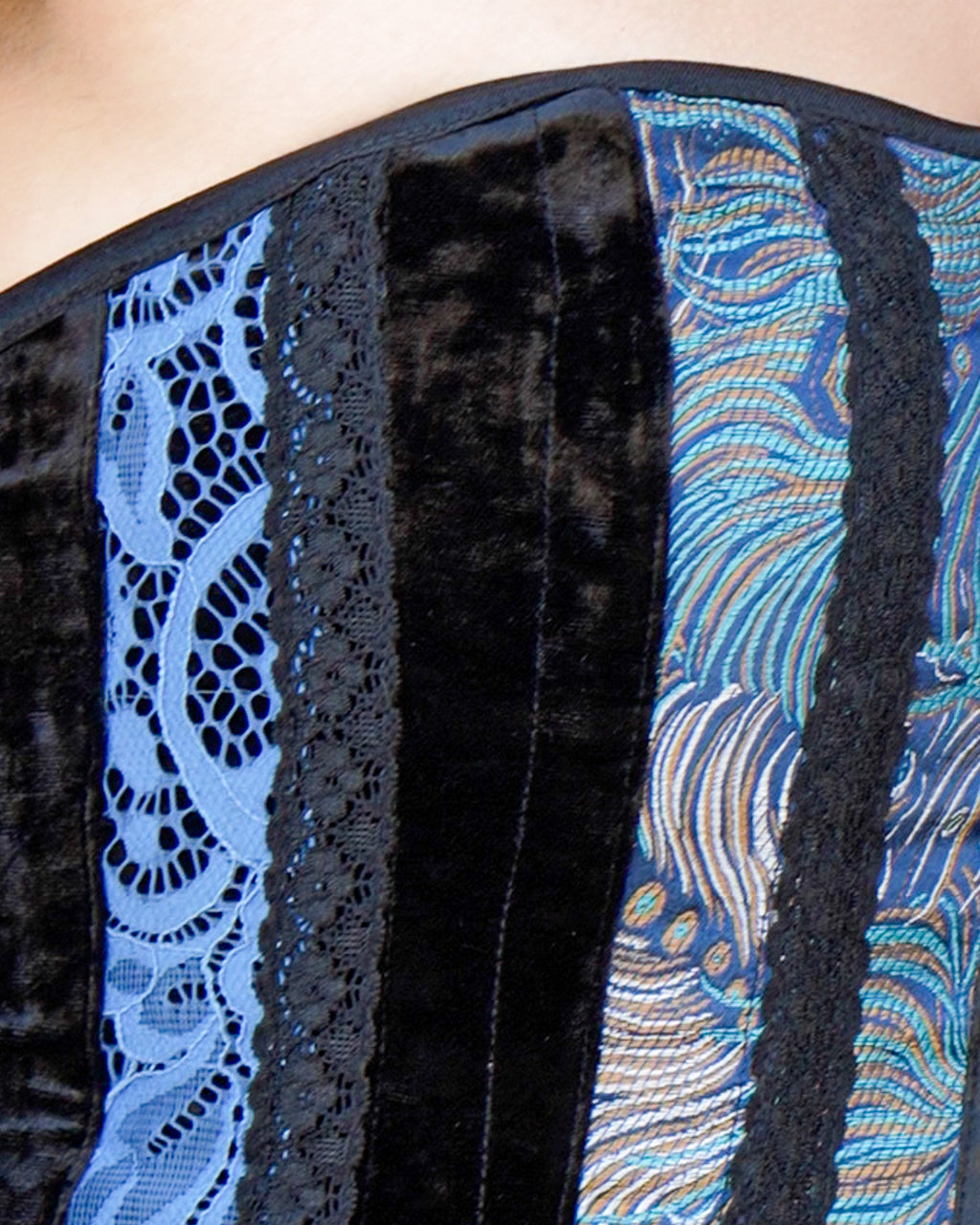 Close-up of a garment featuring vertical panels of black velvet, black lace, and blue patterned fabric with light blue lace.   [style_size:M]