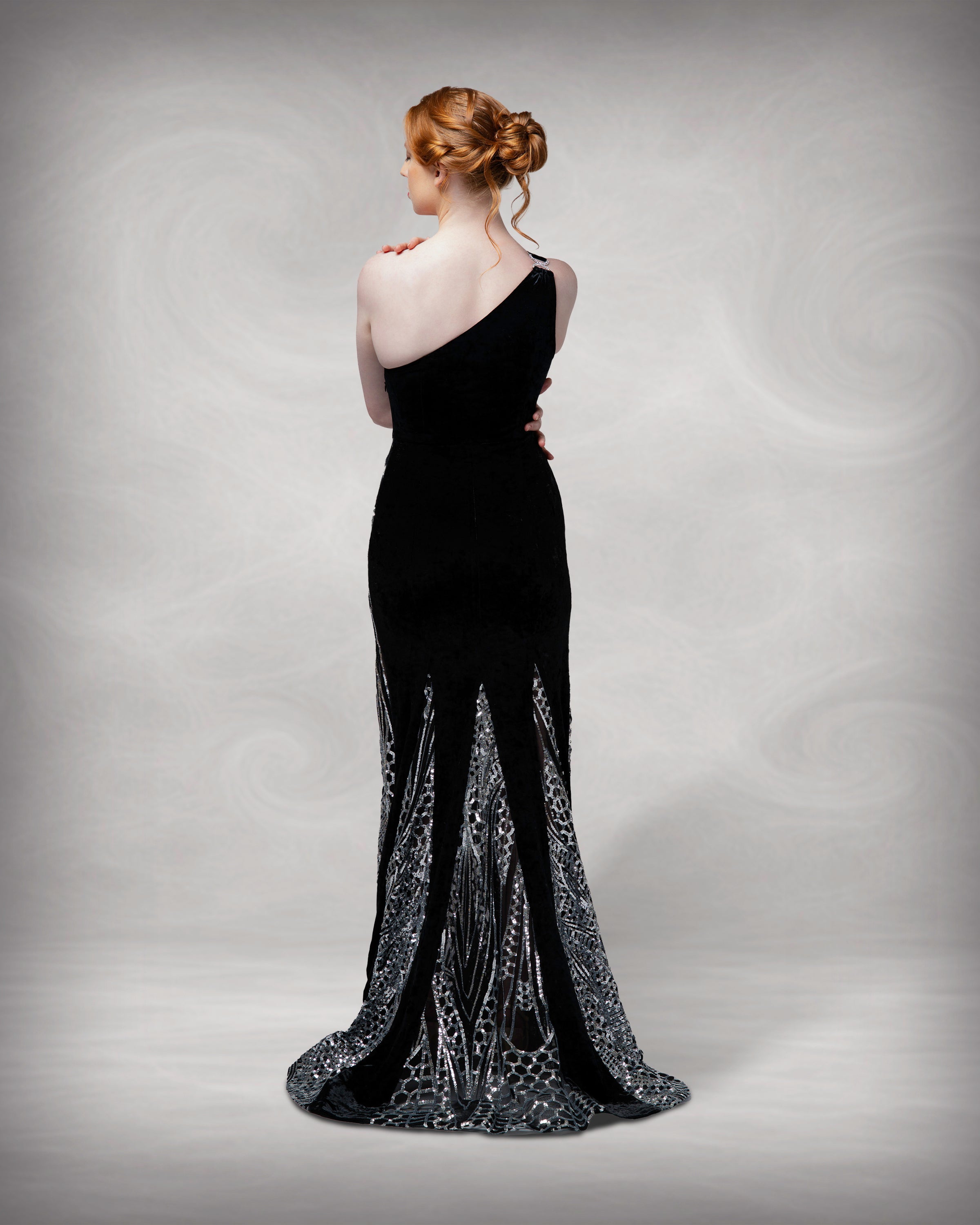 Woman wearing a black evening gown with a subtle pattern on a gray background