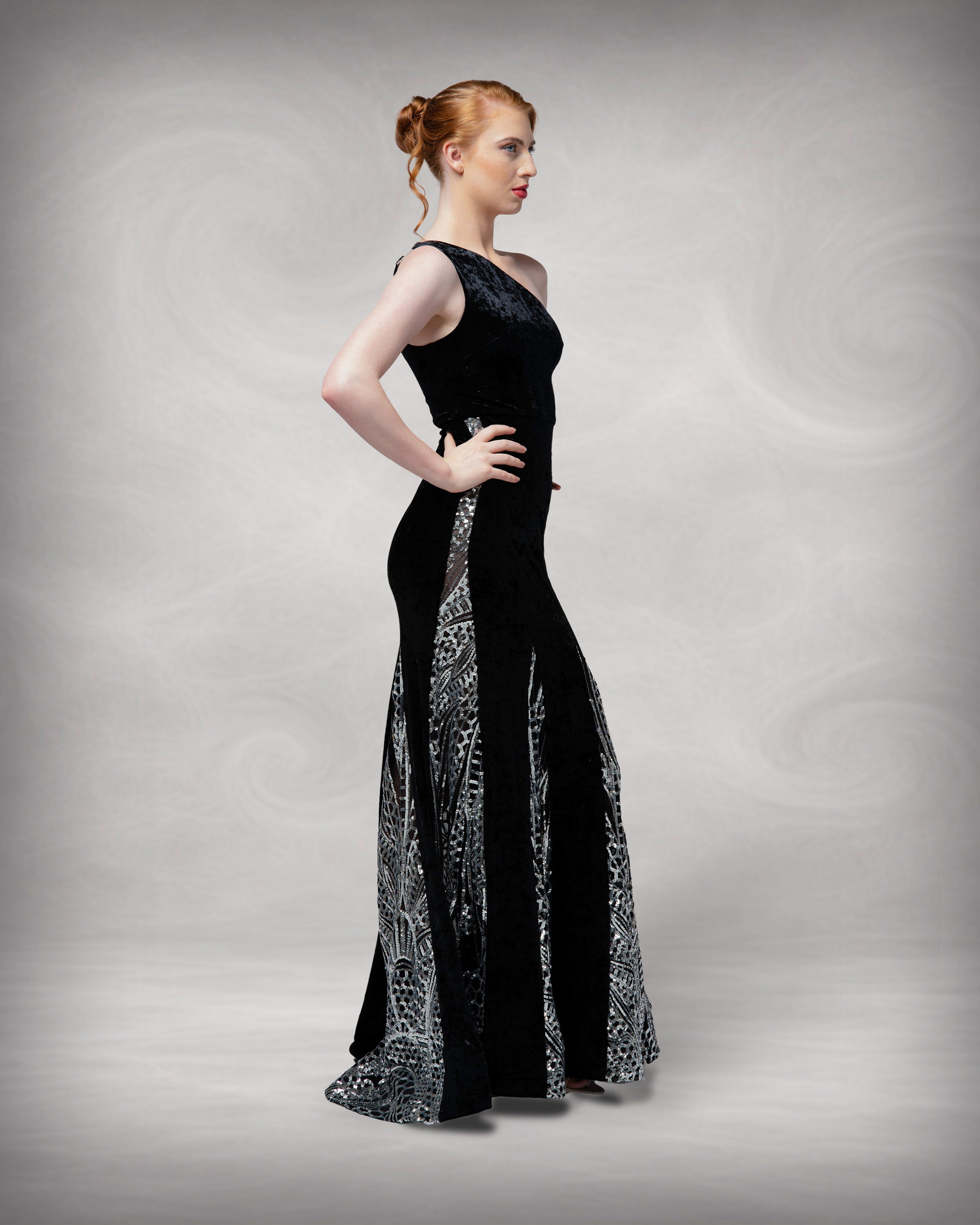 Woman wearing a black evening gown with silver detailing on a gray background