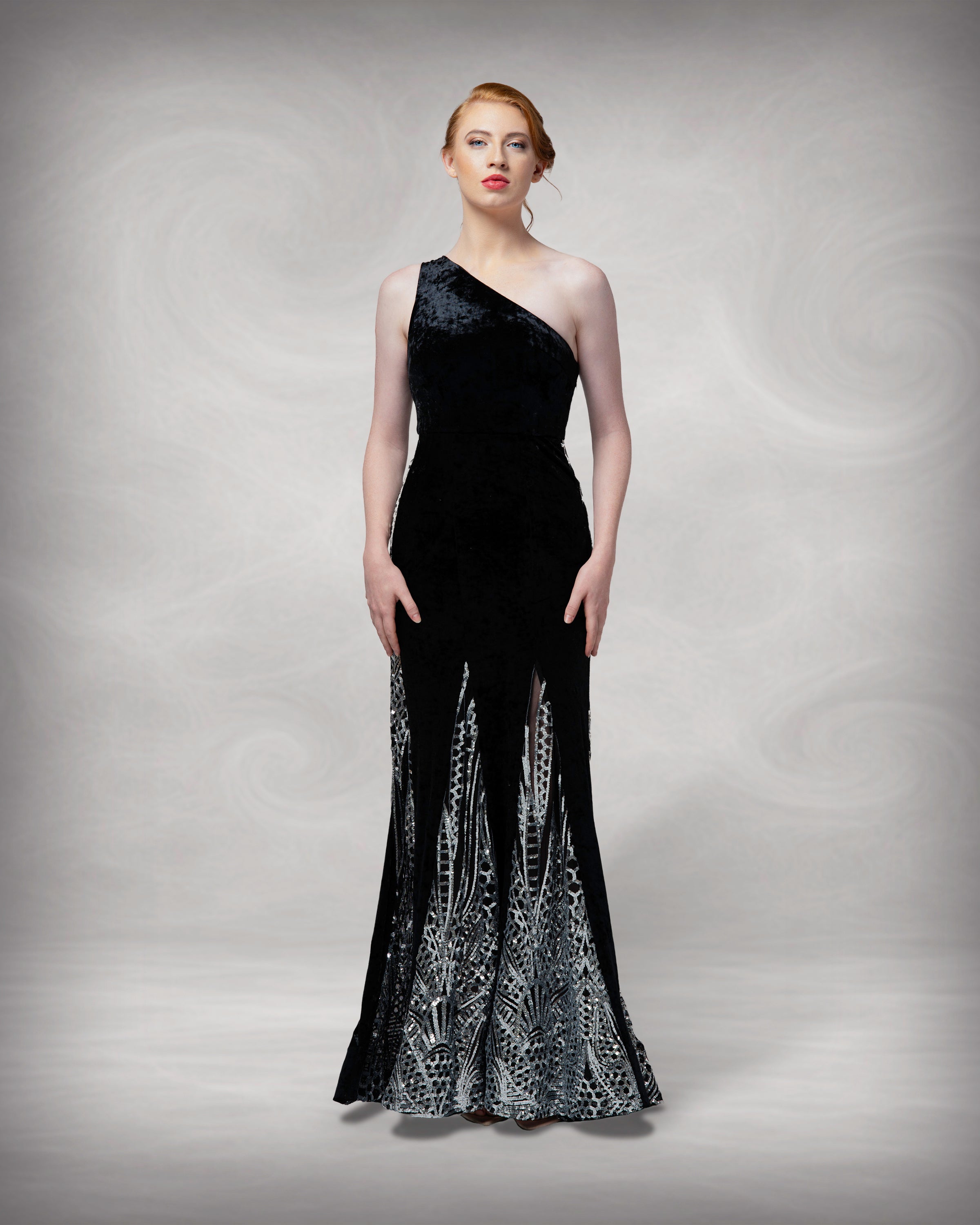 Woman wearing a black one-shoulder evening gown with intricate white detailing on a gray background